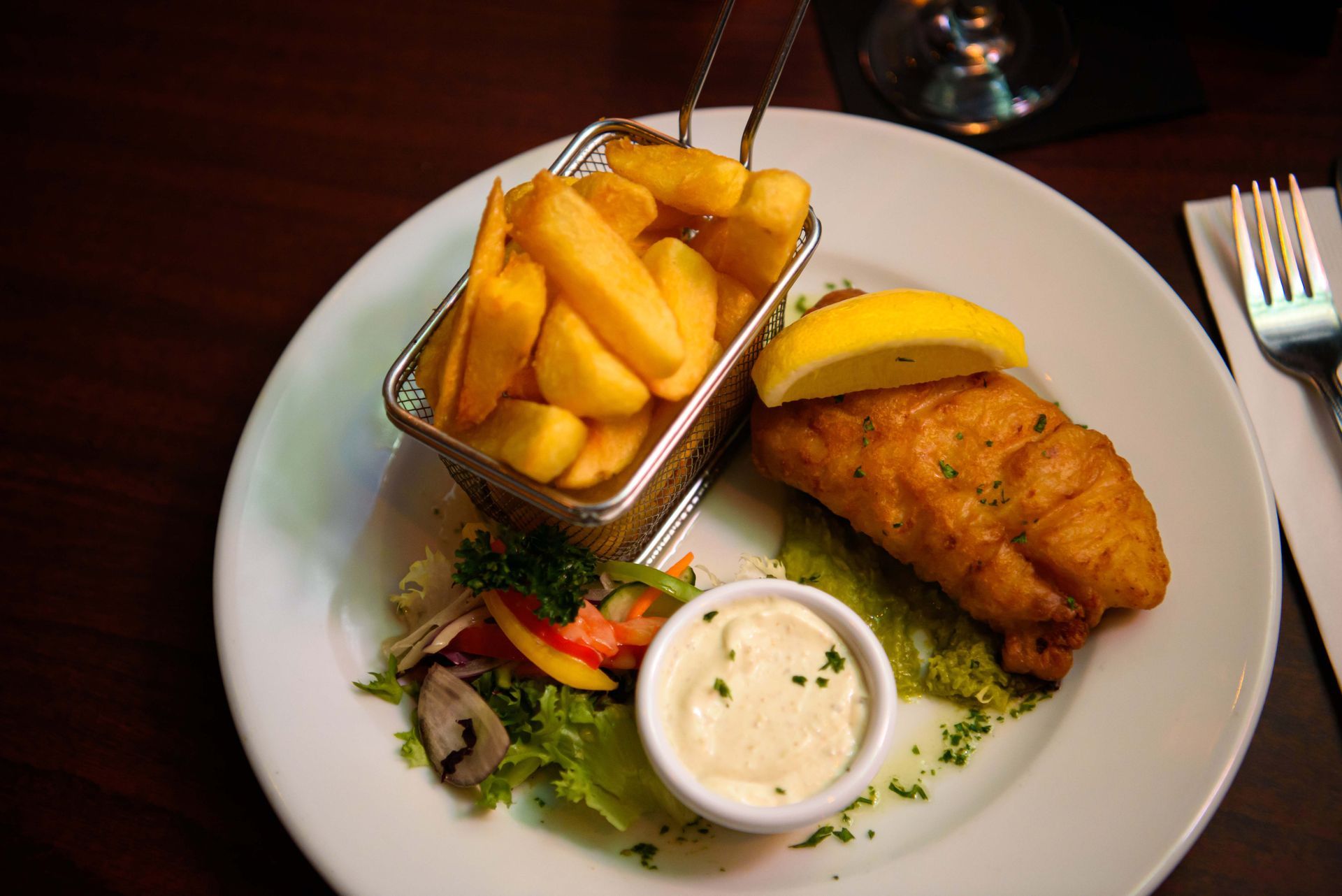 Fish and chips with lemon, salad, and sauce on a white plate.