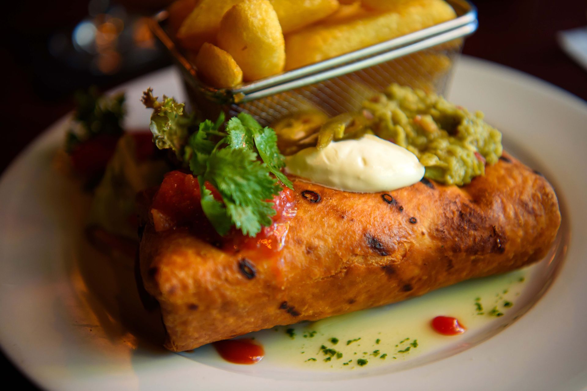 A burrito on a plate with fries, guacamole, and sour cream.