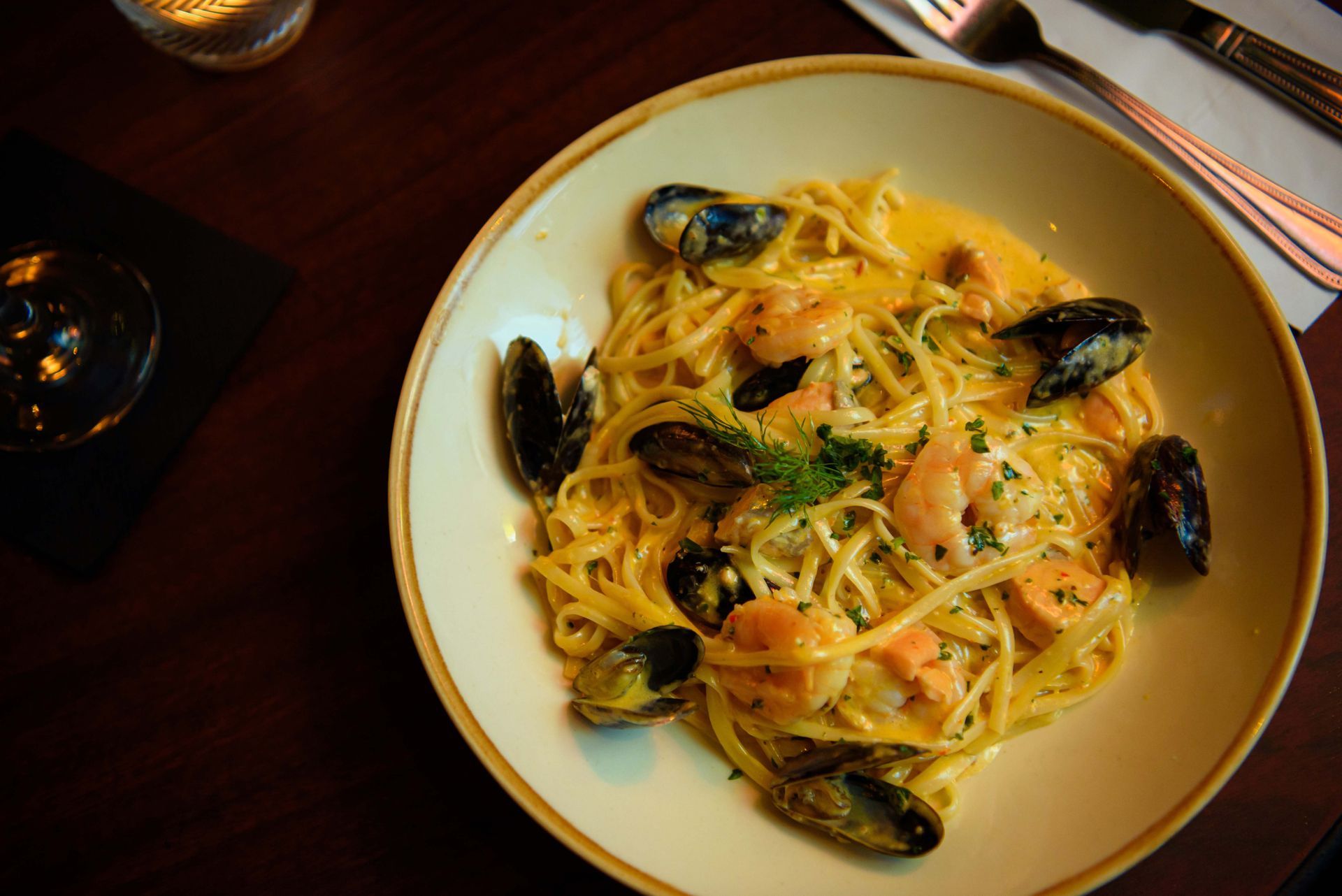 Pasta dish with mussels and shrimp in a creamy sauce, on a beige plate.