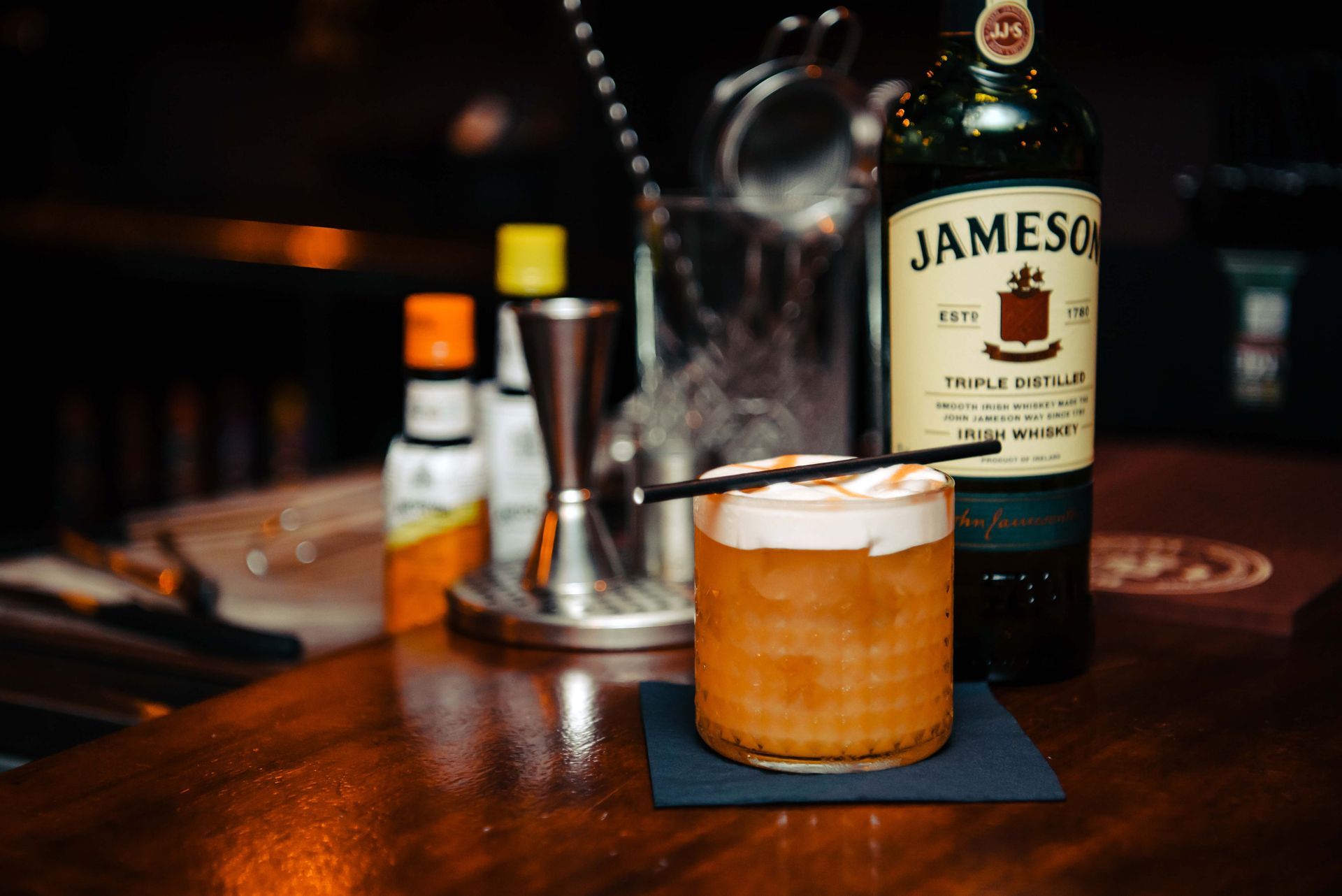 Cocktail with foam on a bar, Jameson bottle in the background.