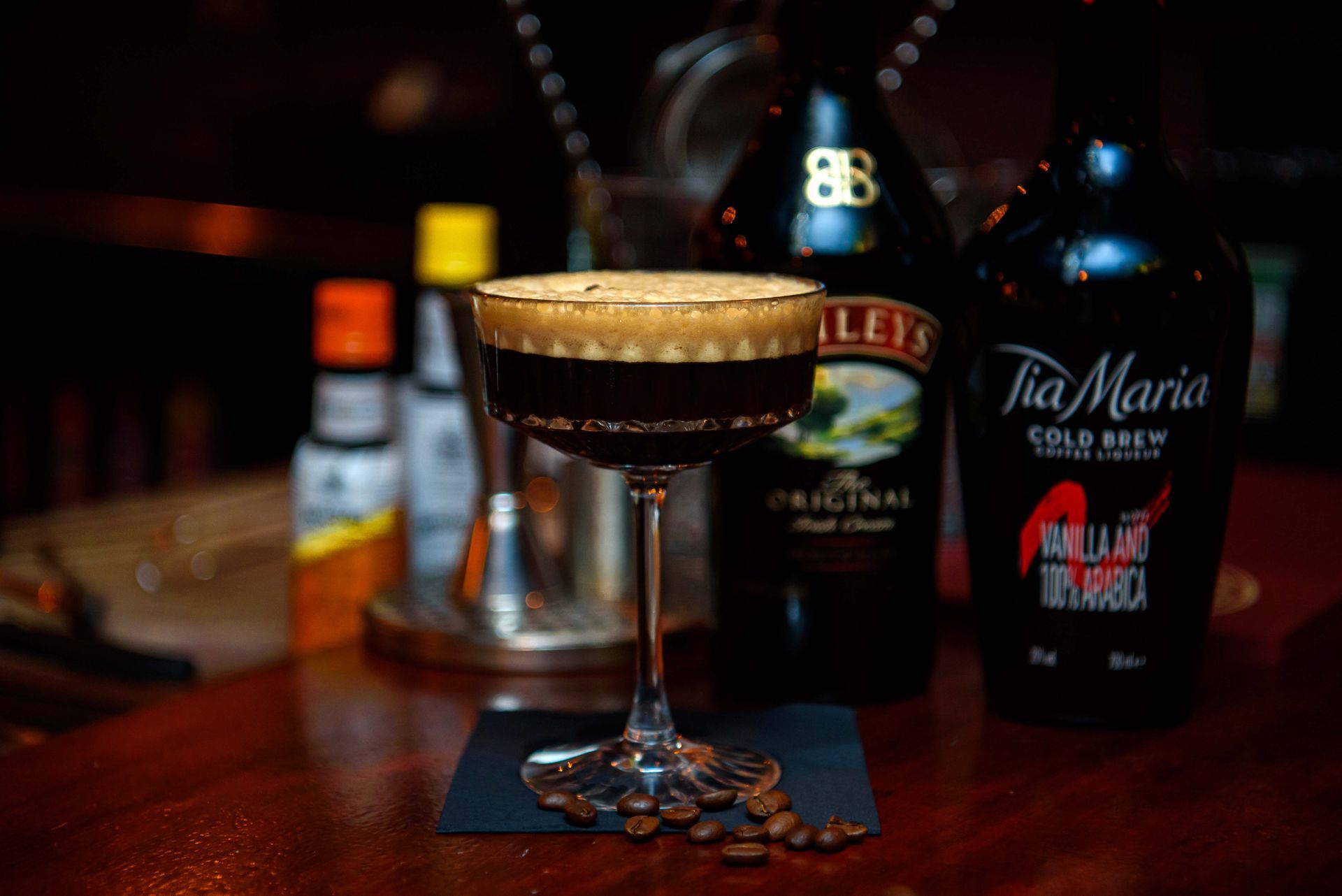 Cocktail in a stemmed glass with a frothy top, surrounded by bottles of coffee liqueur and Irish cream.