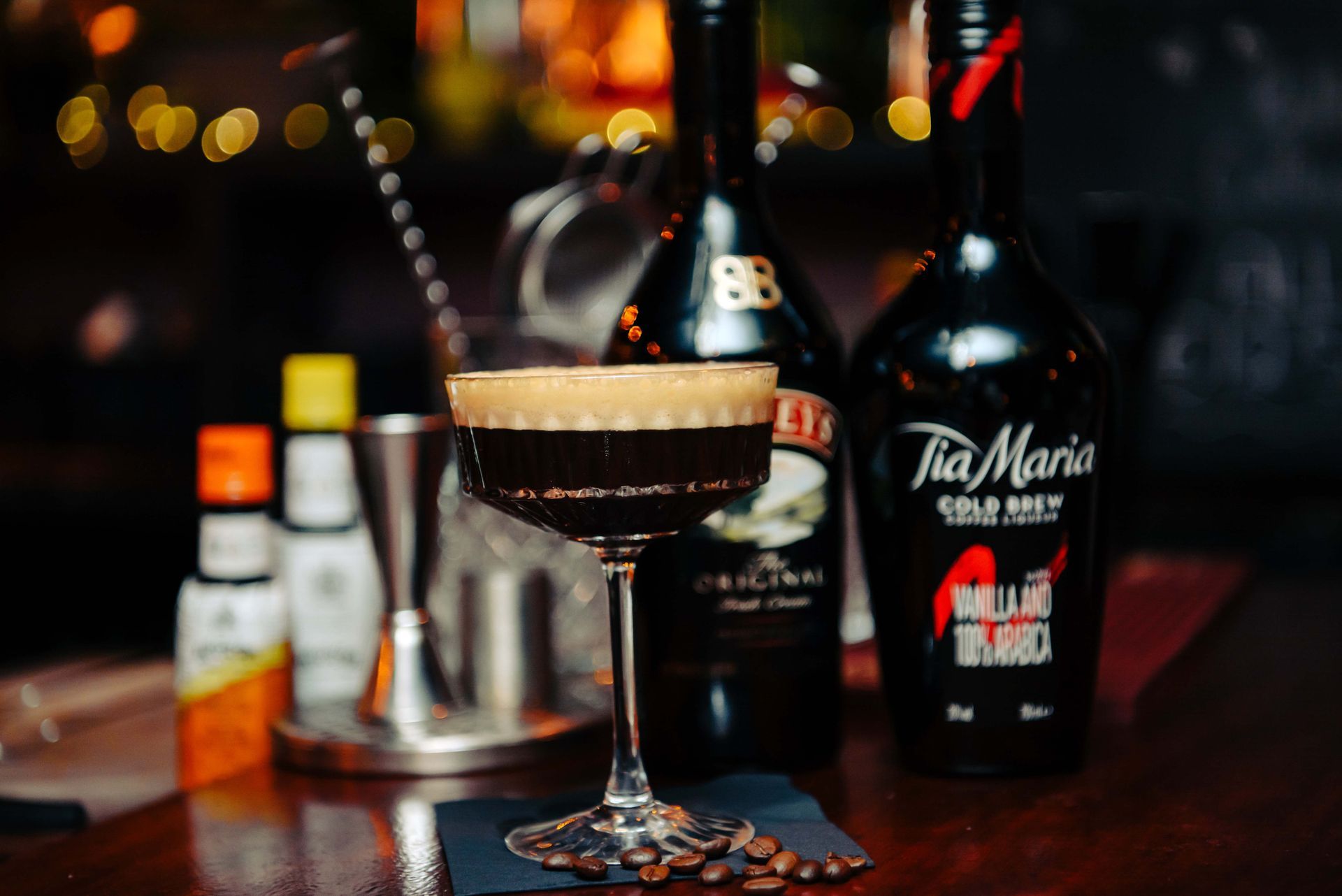 Espresso Martini cocktail in a stemmed glass with bottles of Tia Maria and Baileys in the background.