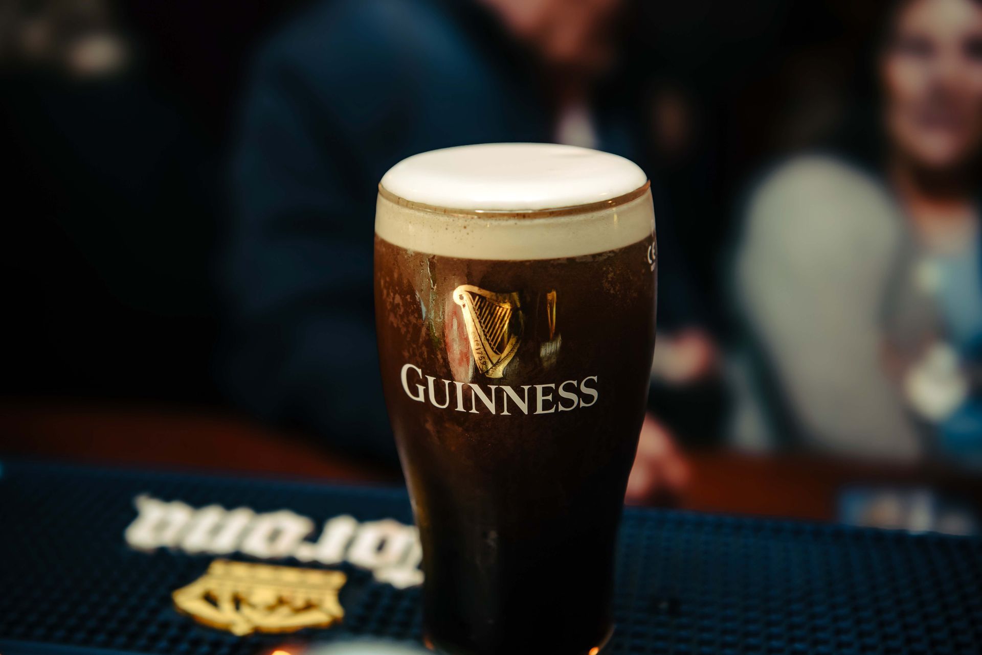Glass of Guinness stout on a bar, creamy head, dark beer, blurry pub background.