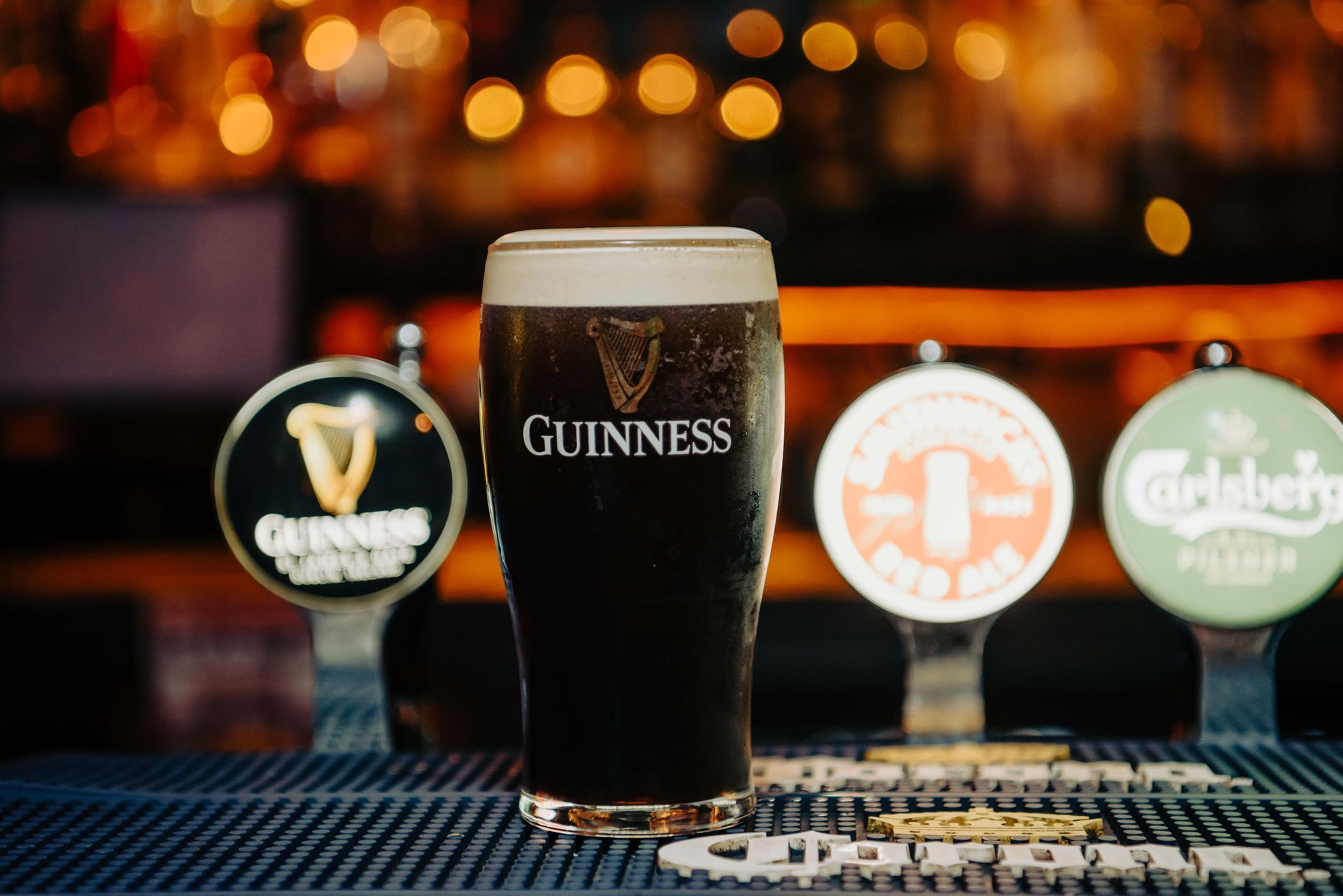 A pint of Guinness stout with a creamy head on a bar, with beer taps behind it.