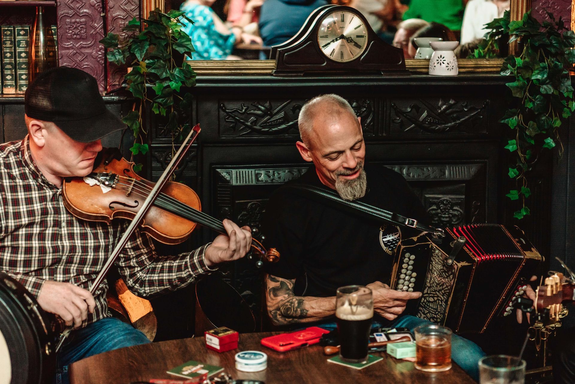Two musicians playing instruments in a pub. One plays a violin, the other an accordion.