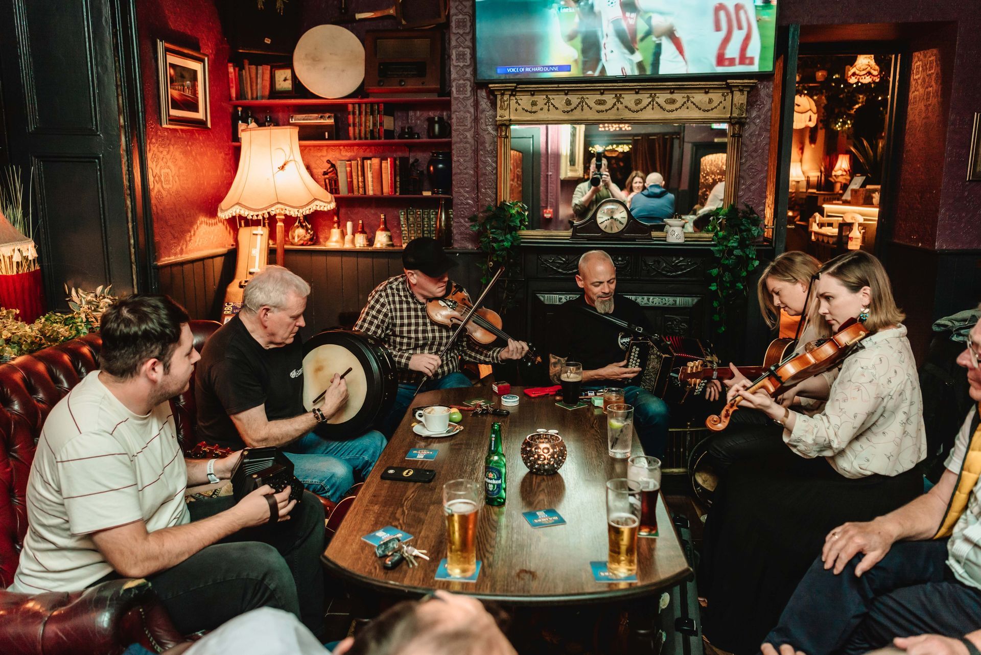 A band plays music in an Irish pub. People sit around a table, watching and listening.