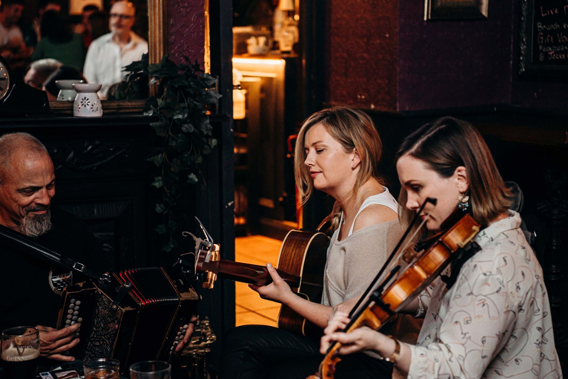 Three musicians playing instruments in a dimly lit bar: accordion, guitar, violin.