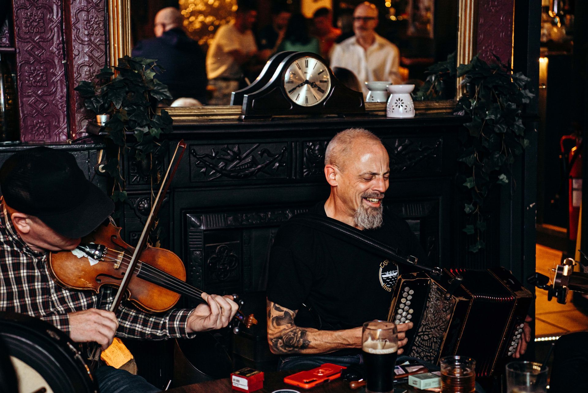 Two musicians perform in a pub: a violinist and an accordion player. The accordion player smiles.