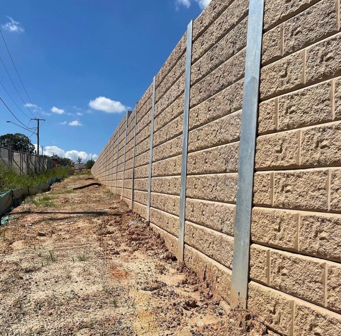 A concrete retaining wall along a dirt road with a blue sky in the background.