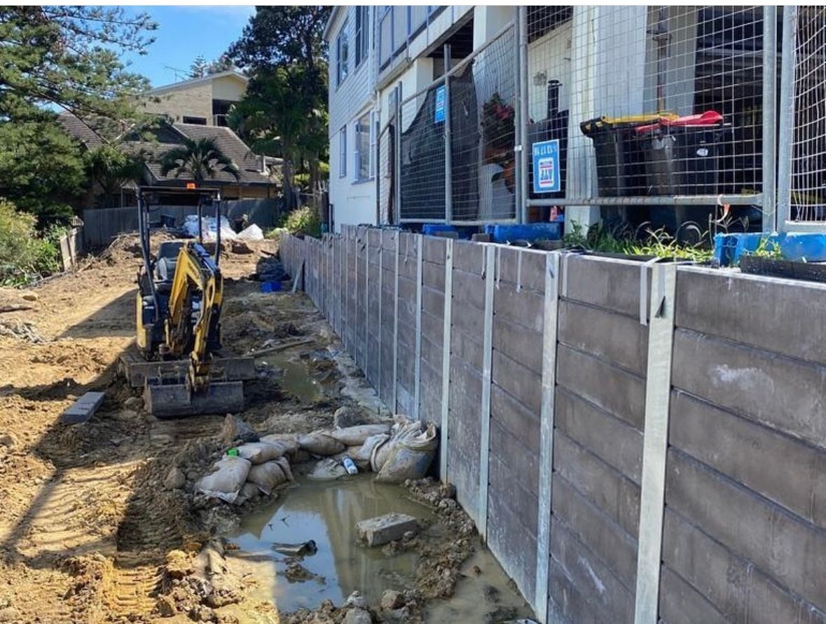 A yellow excavator is digging a hole in the dirt in front of a building.