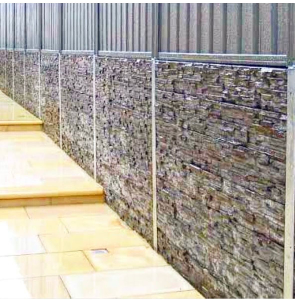 A large brick wall along a dirt road with a blue sky in the background.