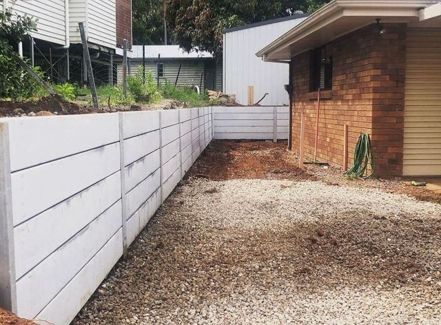 A white fence is surrounding a gravel driveway in front of a brick house.