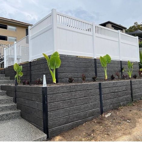 A white fence is sitting on top of a black retaining wall.