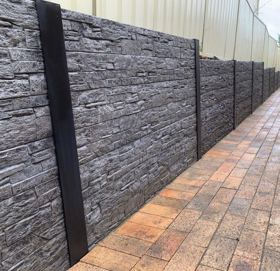 A brick wall along a sidewalk next to a building.