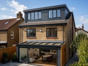 Modern three-story brick house with large glass rear extension and rooftop dormer.