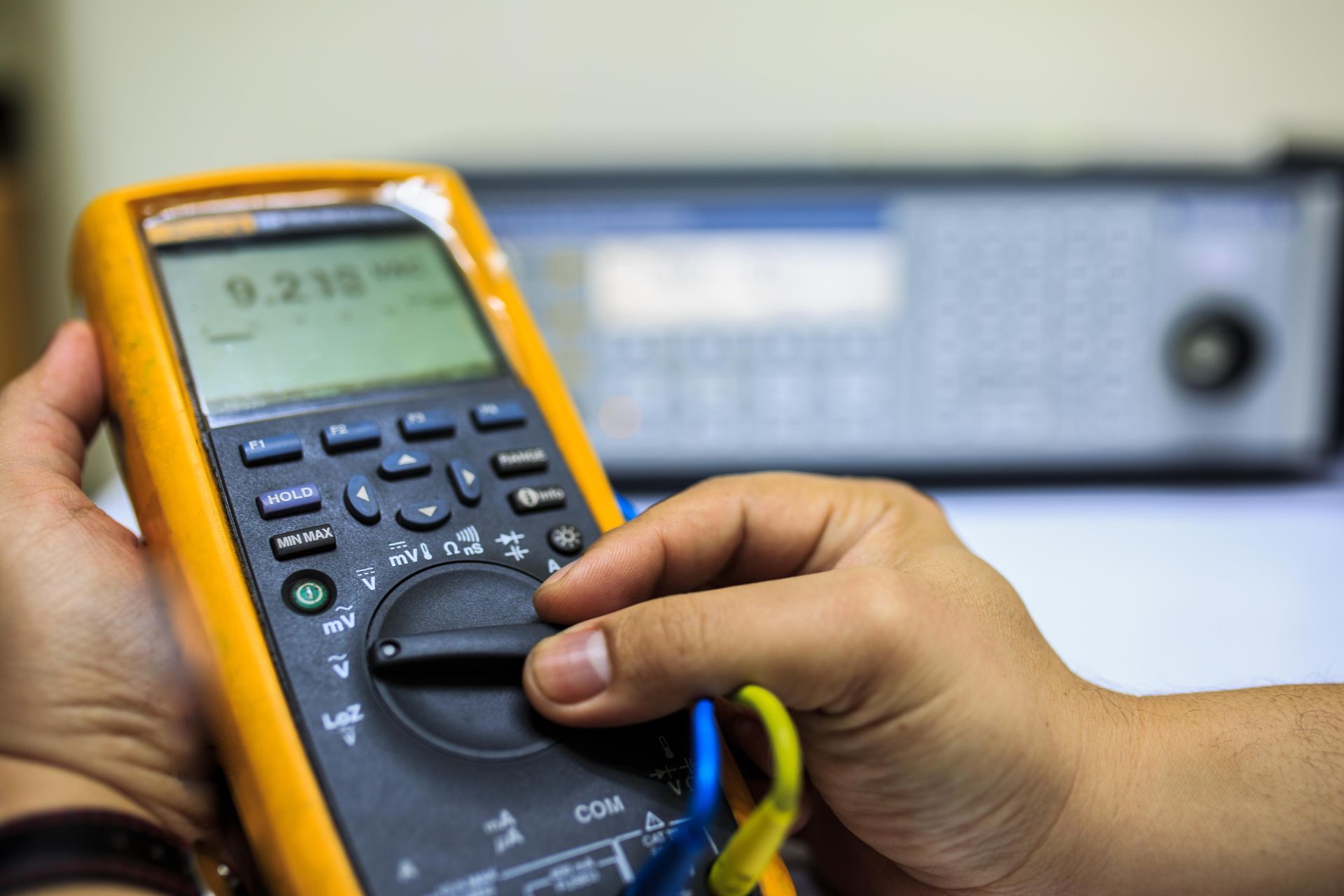 Hand adjusting a digital multimeter dial for electrical measurement in a lab setting.