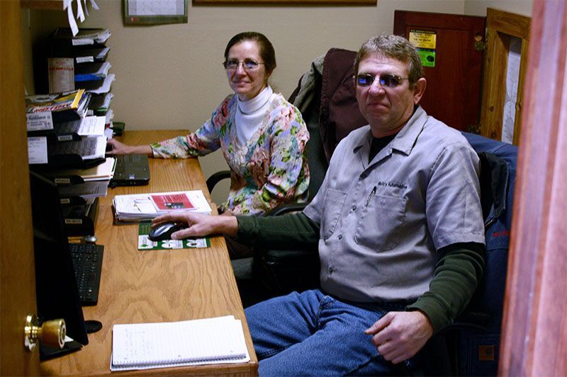 Two people at a desk. Woman in floral top, man in shirt and sunglasses, both looking forward. Office setting. | Mohr's Automotive