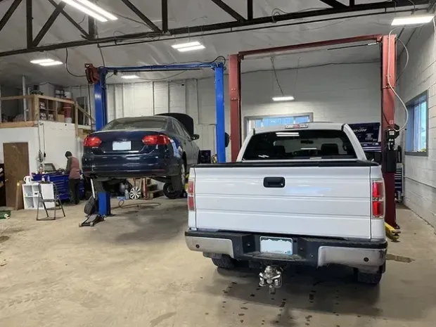 Inside auto shop: Car on lift, white truck, mechanic working, tools, garage setting. | Mohr's Automotive