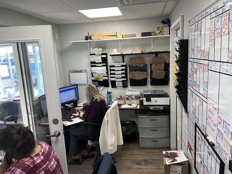 Two people working in a small office with a whiteboard, desk, and computer. | Mohr's Automotive