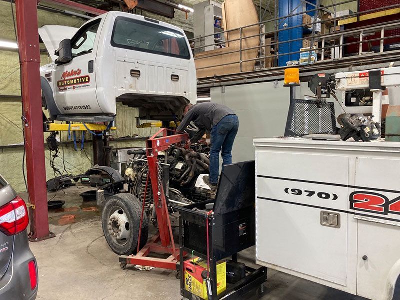 Mechanic working on a truck engine in a garage. The truck is elevated. A cabinet is on the right. | Mohr's Automotive