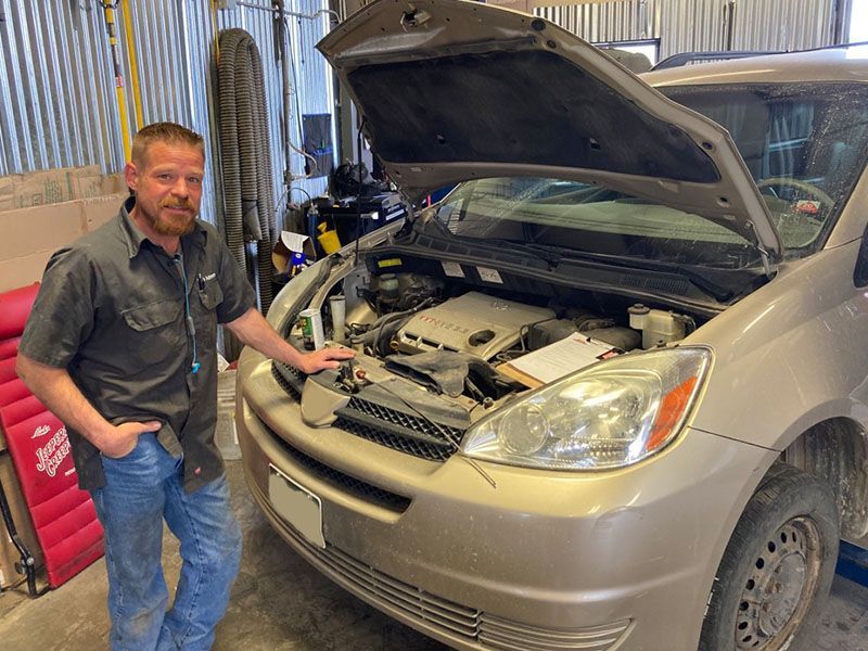 Mechanic standing next to a car with an open hood in a garage. | Mohr's Automotive