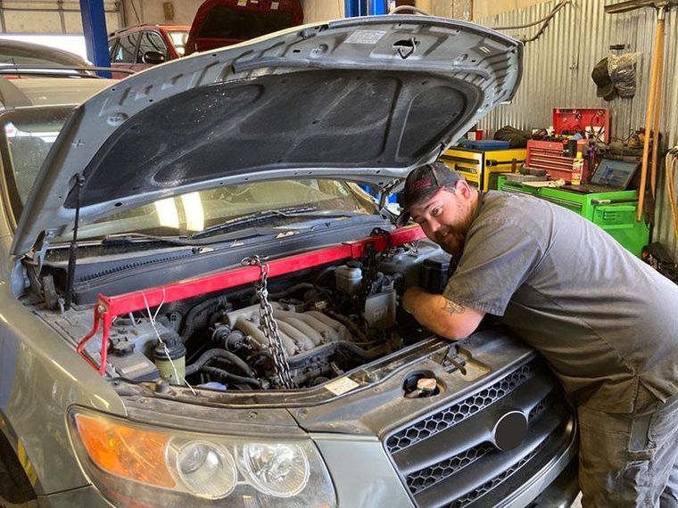 Mechanic working on car engine, leaning over the open hood in a garage. Red support bar in place. | Mohr's Automotive