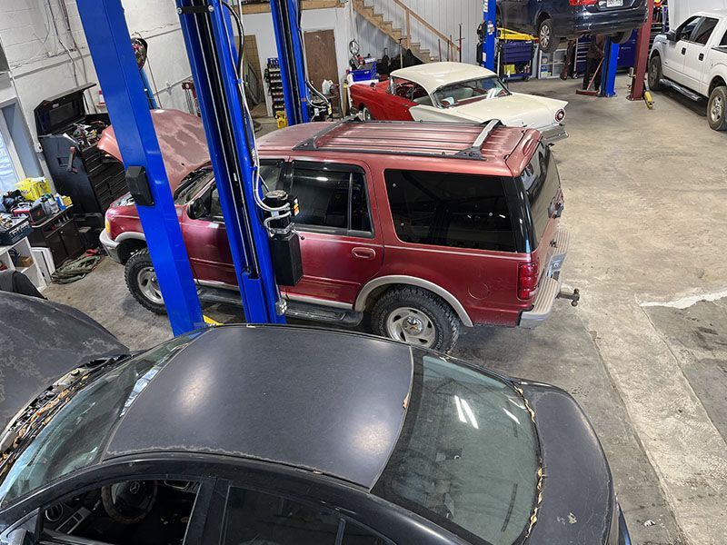 Red SUV and black car in a repair shop, other vehicles, a lift, and equipment are visible. | Mohr's Automotive