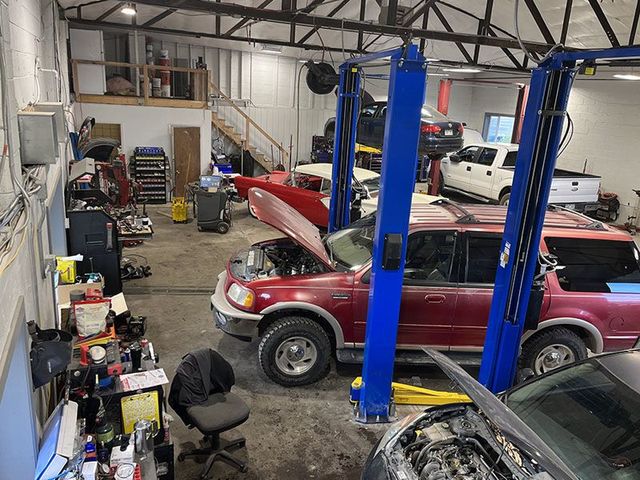 Interior of a car repair shop with several vehicles, including a red SUV on a lift. Tools and equipment are visible. | Mohr's Automotive