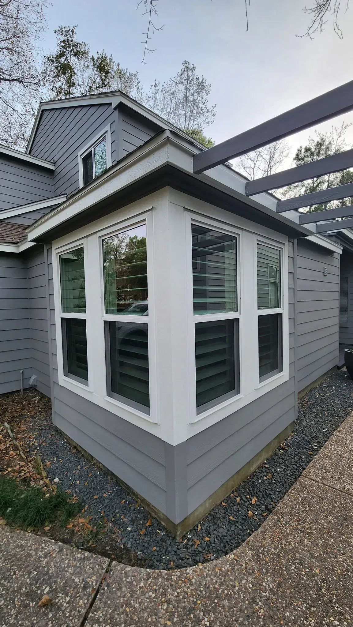 Grey house with white trim bay window, pergola.