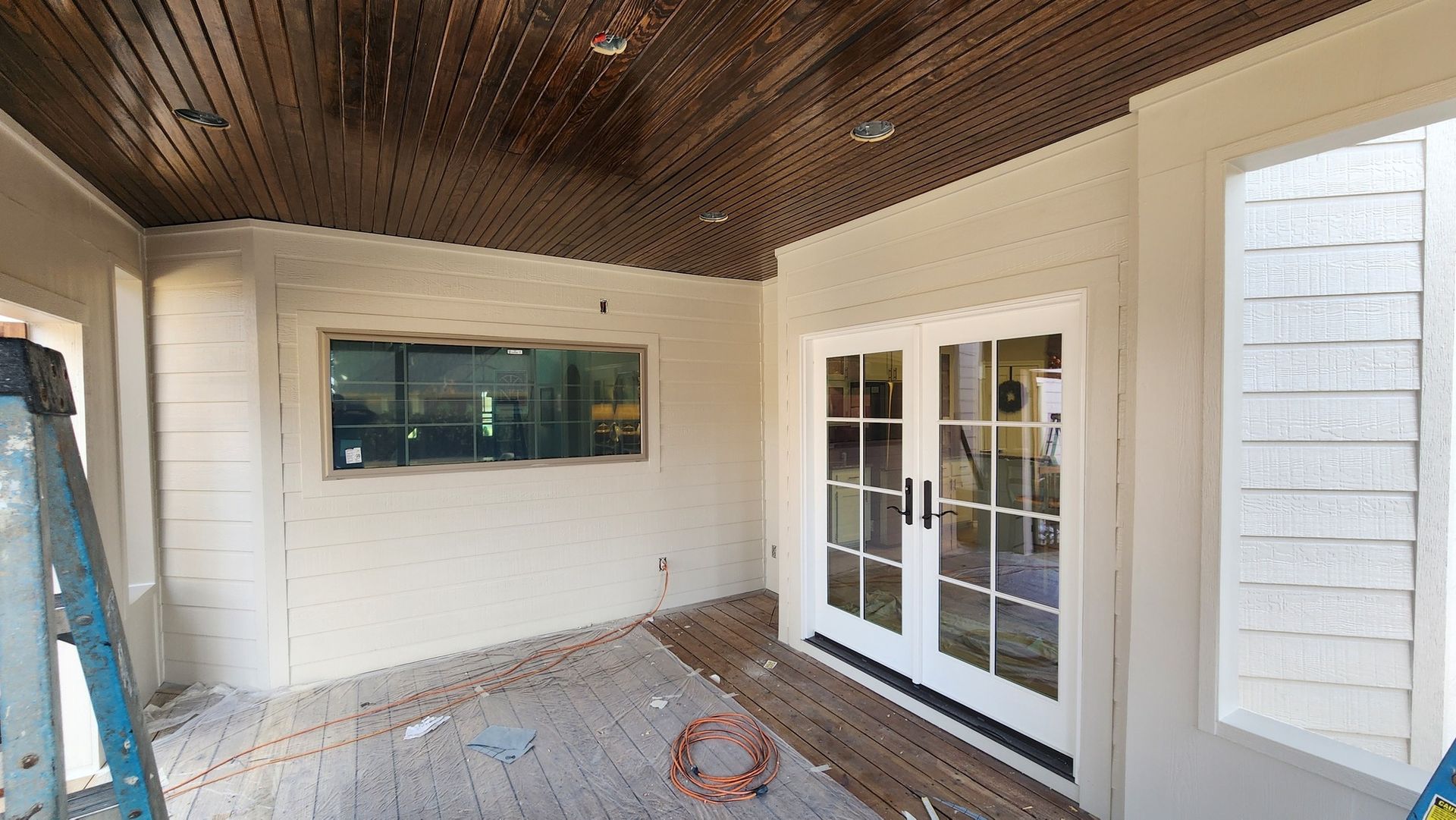 Interior view of a room under construction with white walls, French doors, and a wooden ceiling.