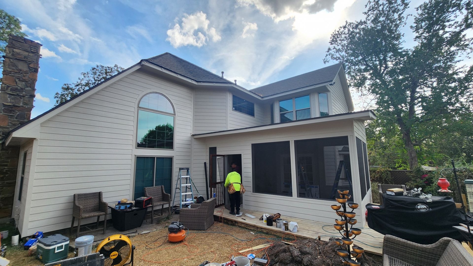 House exterior with two-story section and screened porch, cloudy sky. Man stands near open door.