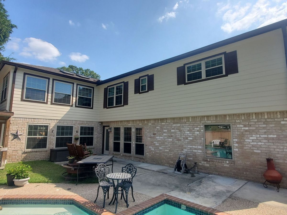 Back exterior of a two-story beige and brick house with windows and a small patio area with a pool.