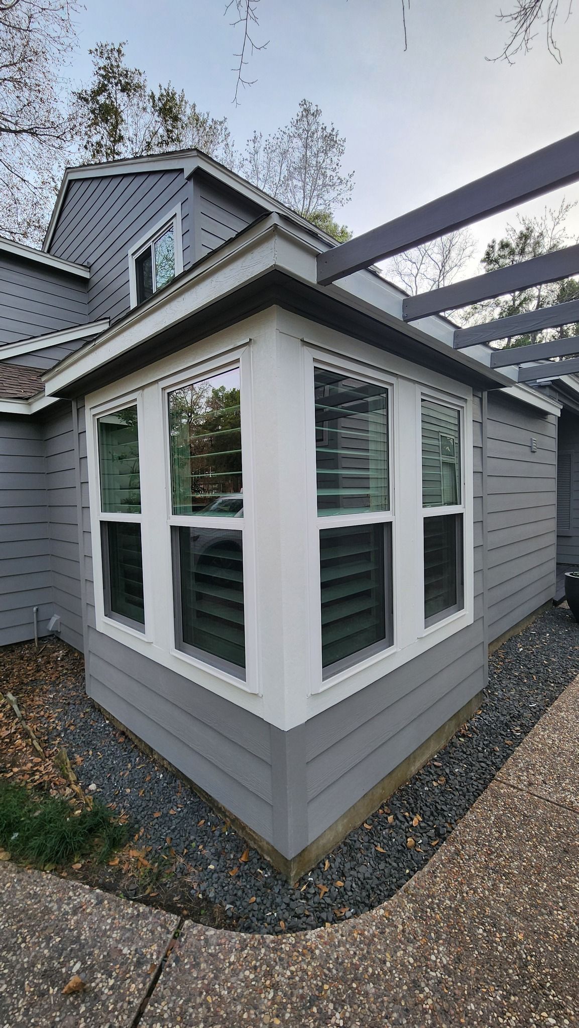 Gray house with white window frames and a black pergola.