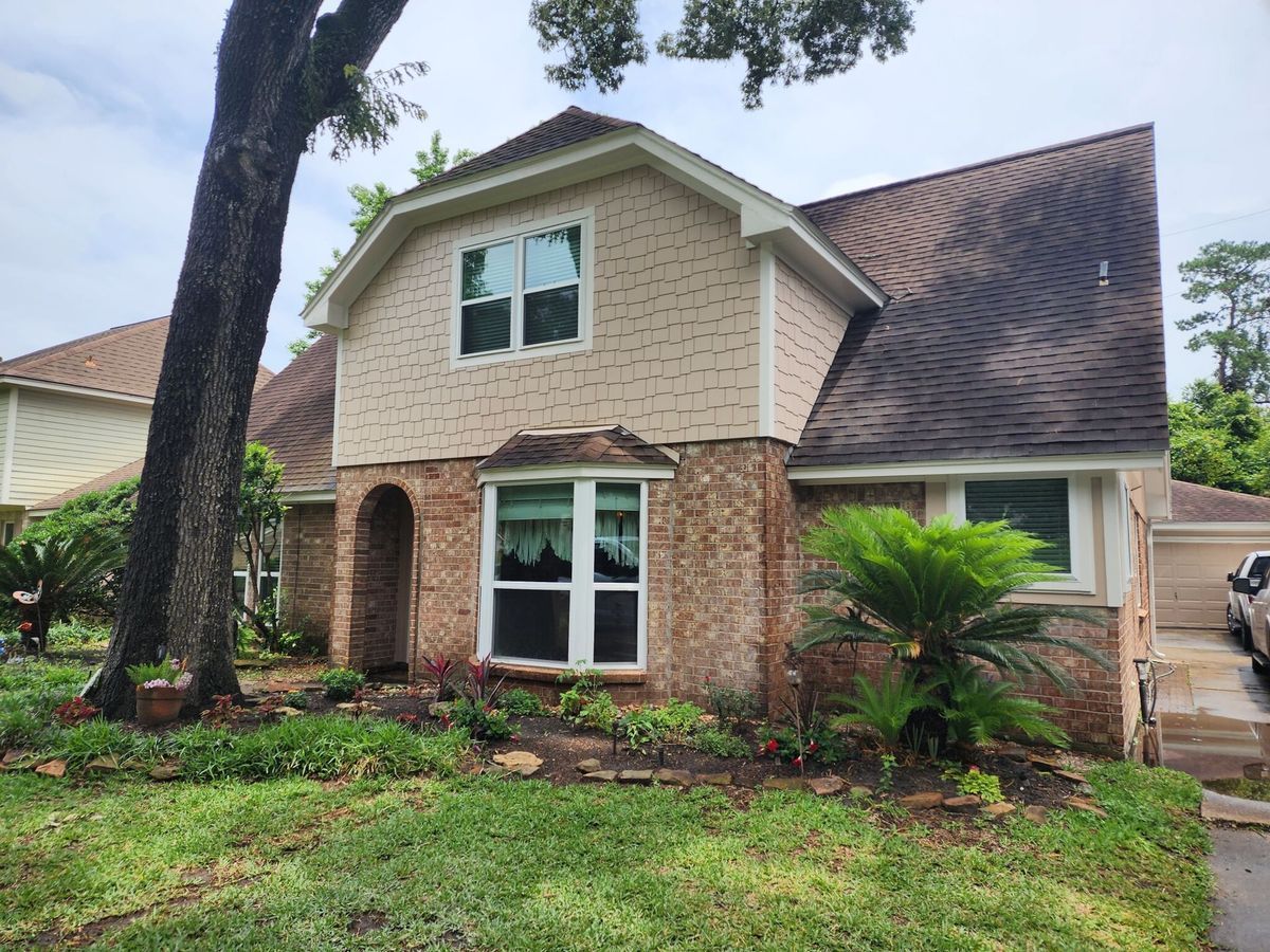 Two-story house with brick and tan siding, brown roof, and lush green landscaping.