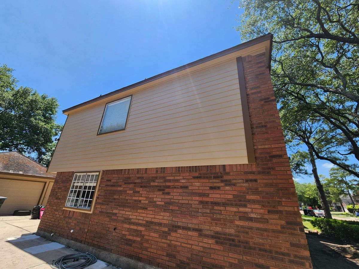 Two-story building with brick bottom, beige siding, and two barred windows against a blue sky.