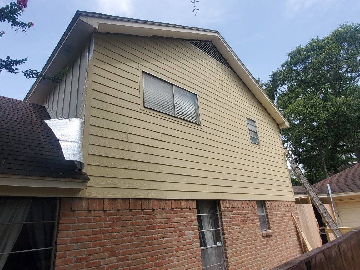 Side view of a house with brick and tan siding, two windows, and dark roof.
