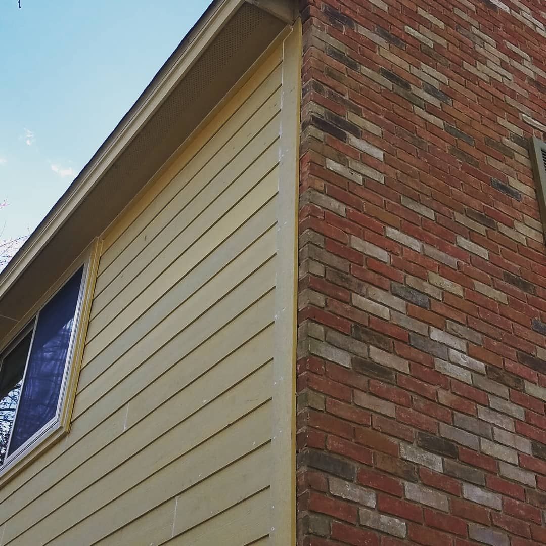 Corner of a building with yellow siding and red brick. A window is visible.