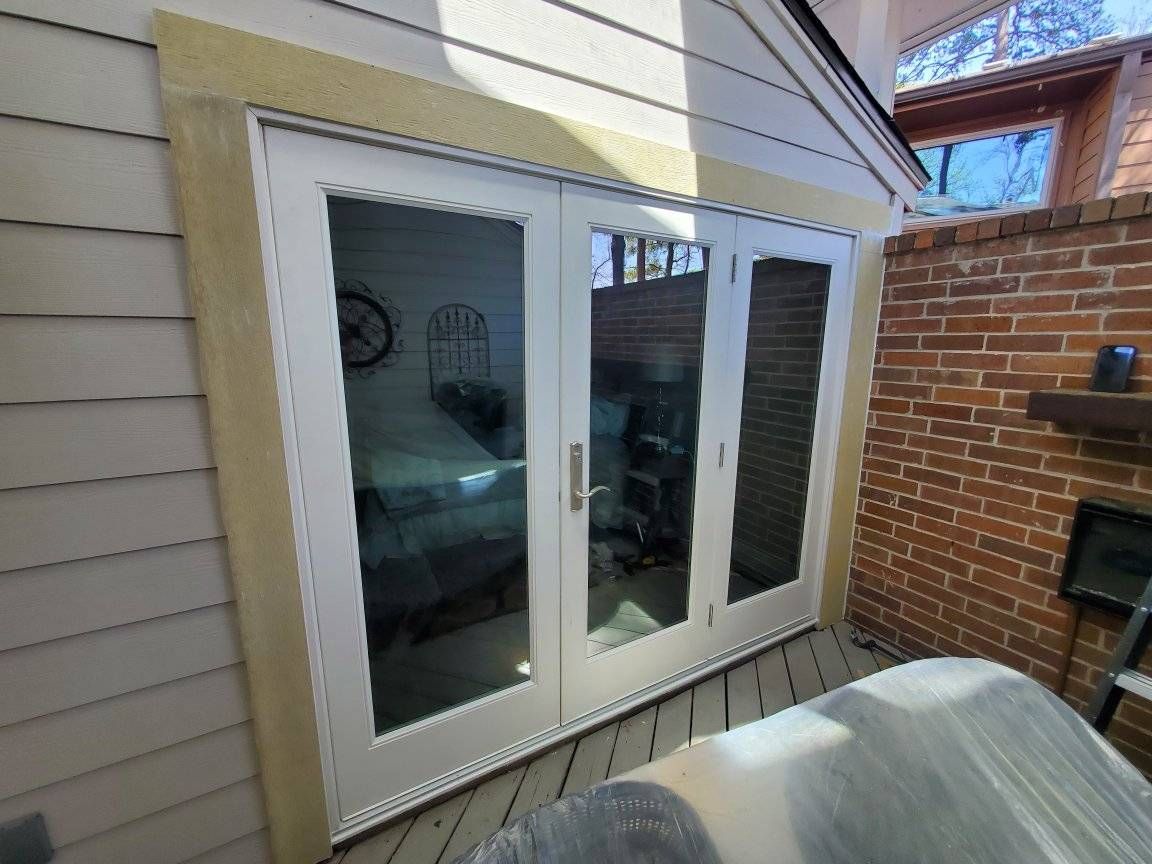 French doors with glass panels, set in a wood frame, open onto a deck. Red brick wall is to the right.