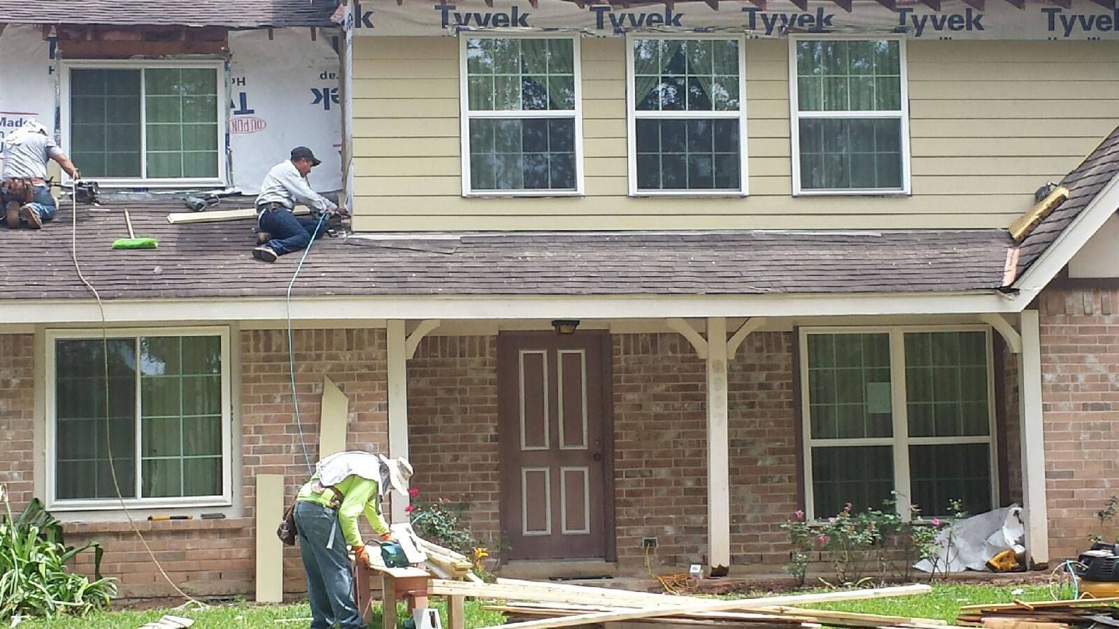 Roofers working on a two-story house with beige siding, replacing roof shingles.