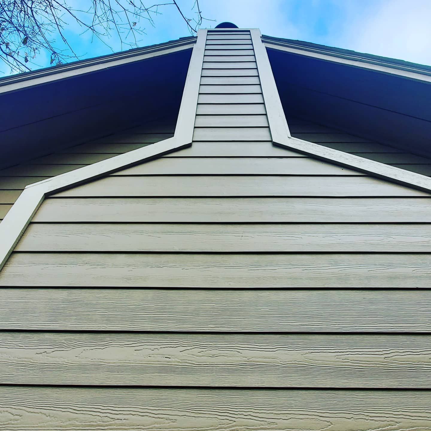 Close-up of a house exterior with horizontal siding in shades of green/gray and a white-trimmed chimney against a blue sky.