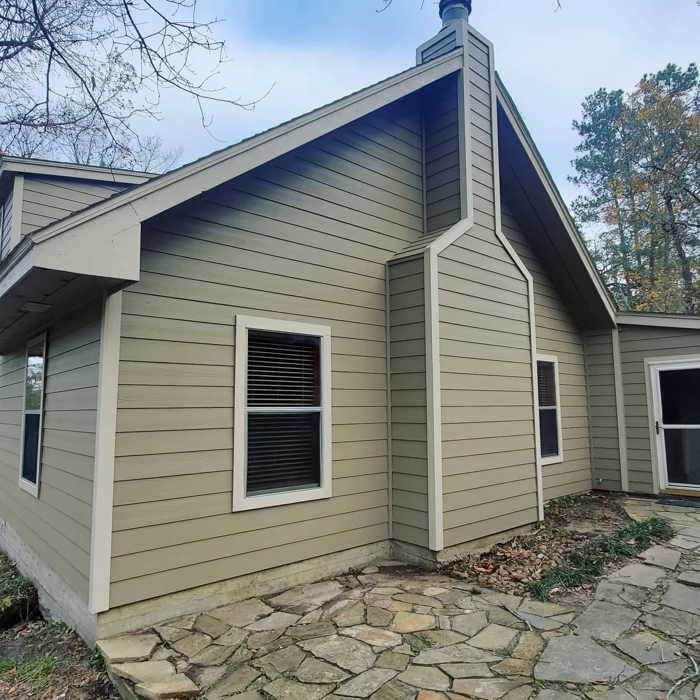 Exterior of a house with light green siding and a stone patio. A chimney and windows are visible.