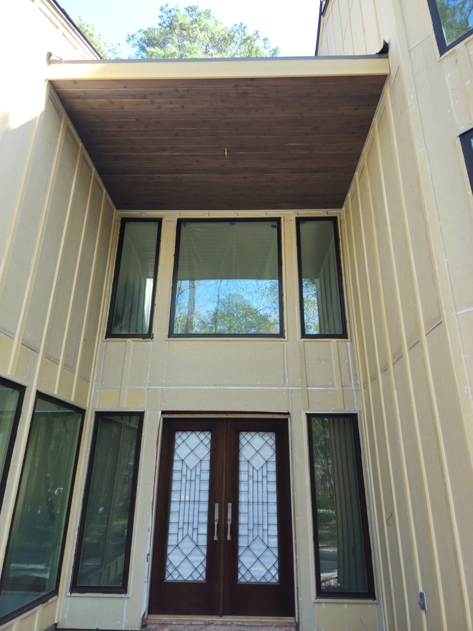 Beige home entrance with double doors, sidelights, and overhead brown overhang.