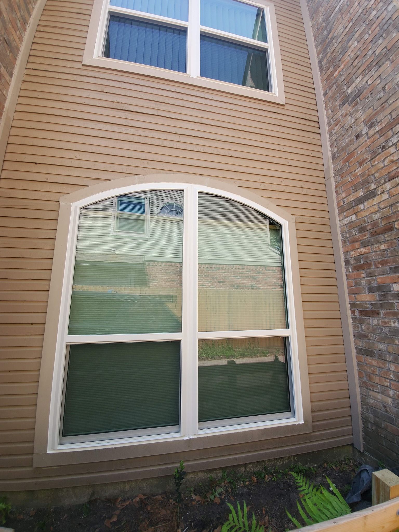 Tan siding with two white-framed windows, one arched, on a building exterior.