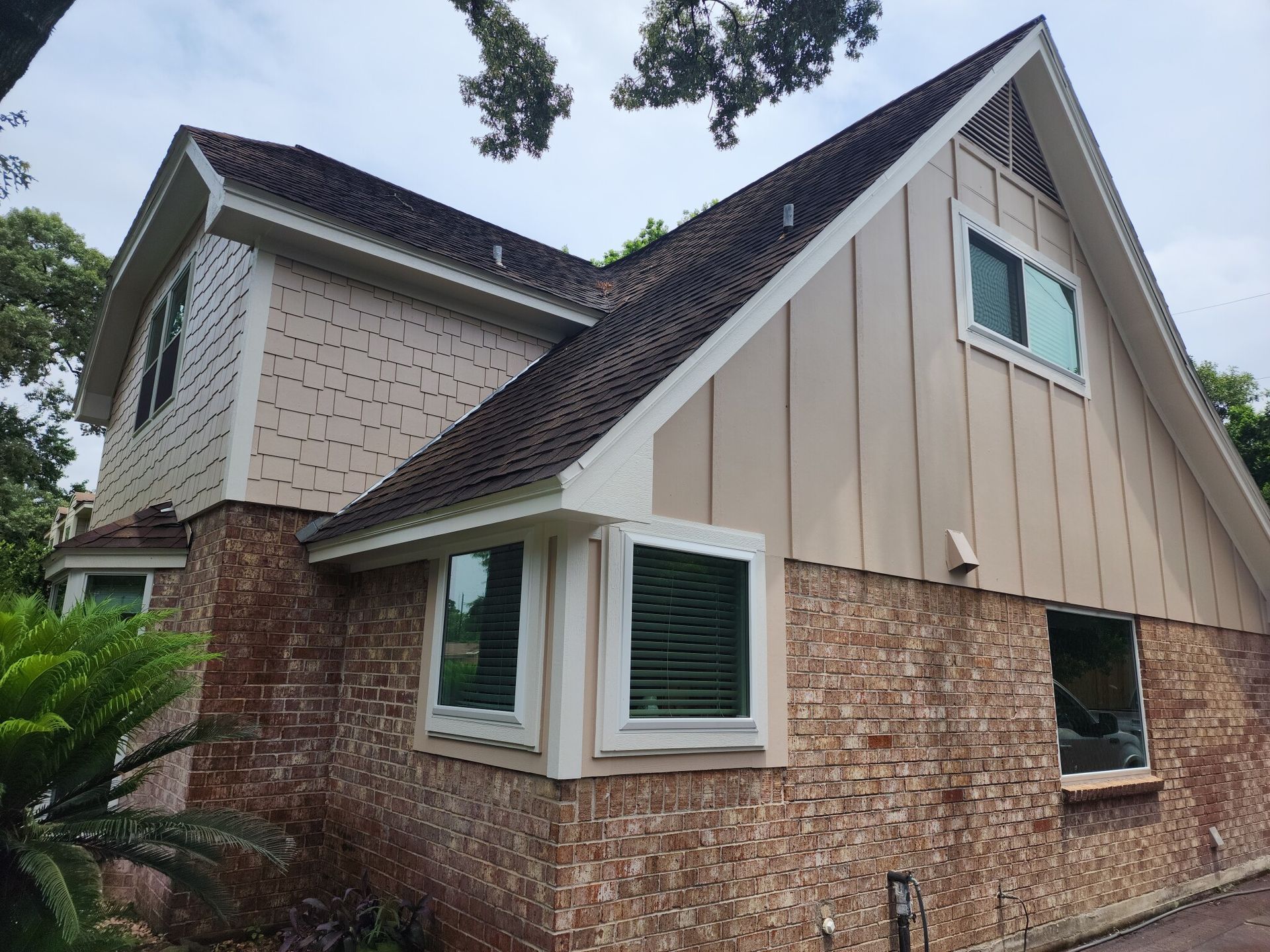 Two-story house with brick and tan siding, brown roof, and multiple windows.