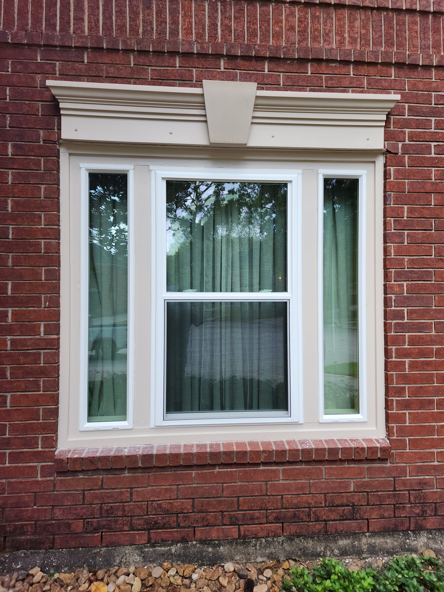 Brick building with a white-framed window. Beige trim and decorative molding. Green curtains are visible.