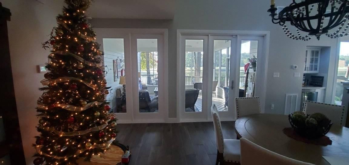 Christmas tree with lights, ribbon, and ornaments in a room with a dining table and doors.