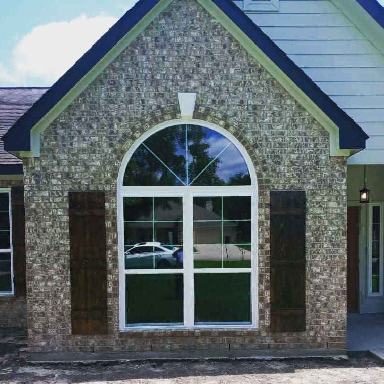 Brick house exterior with arched window, dark shutters, and a dark roof.