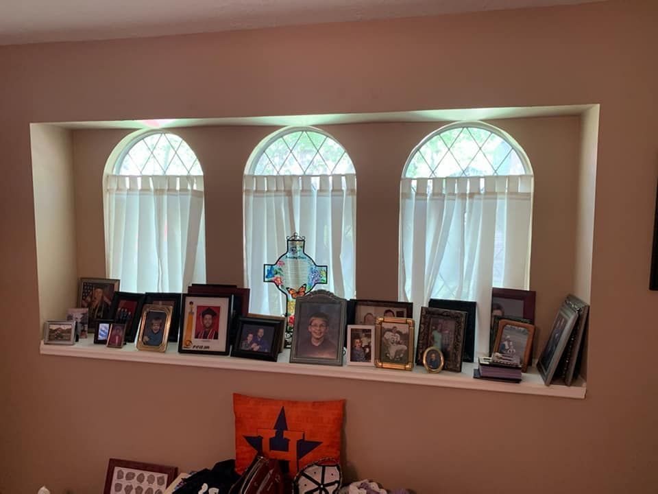 Recessed alcove with three arched windows, each with white curtains. Photos and a cross are on a shelf.