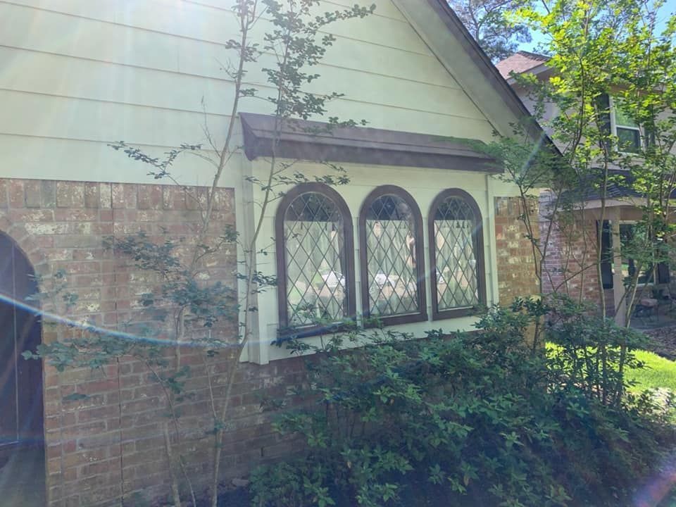 Side of a beige house with three arched windows. Brick and greenery are also visible.
