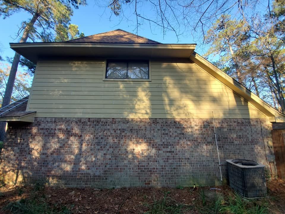 Side view of a house with brick and green siding, set among trees.